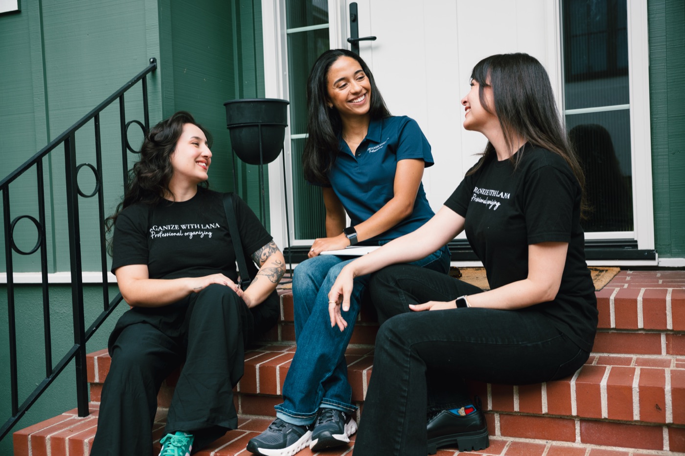 Three Organize with Lana team members sitting together on a client's front steps, laughing between jobs